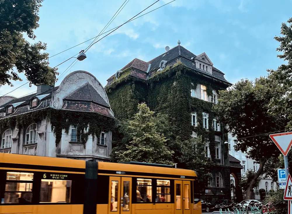 A yellow tram passing a tall, ivy-covered building